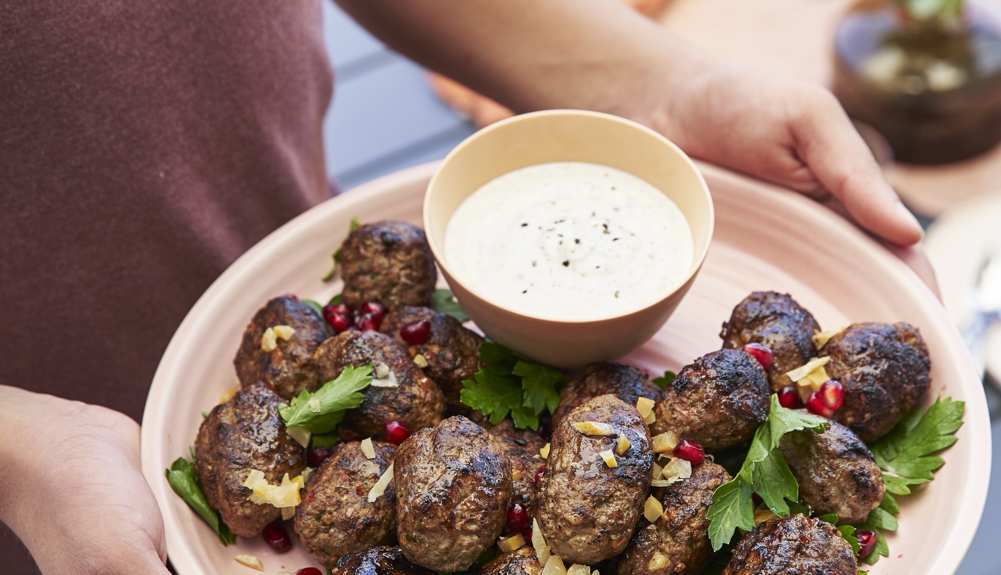 A shared plate of grilled lamb koftas passed around an outdoor table